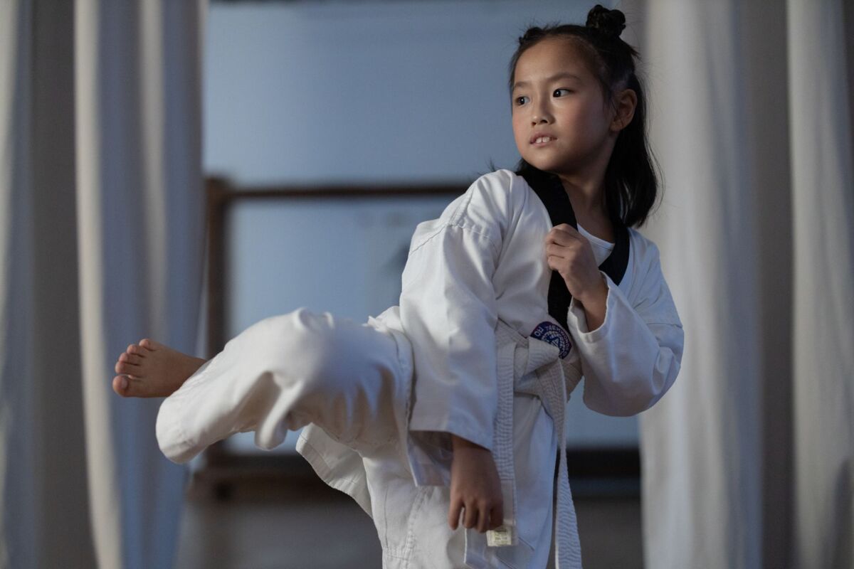 A young girl in a dobok practicing a taekwondo kick indoors, showcasing martial arts skills.