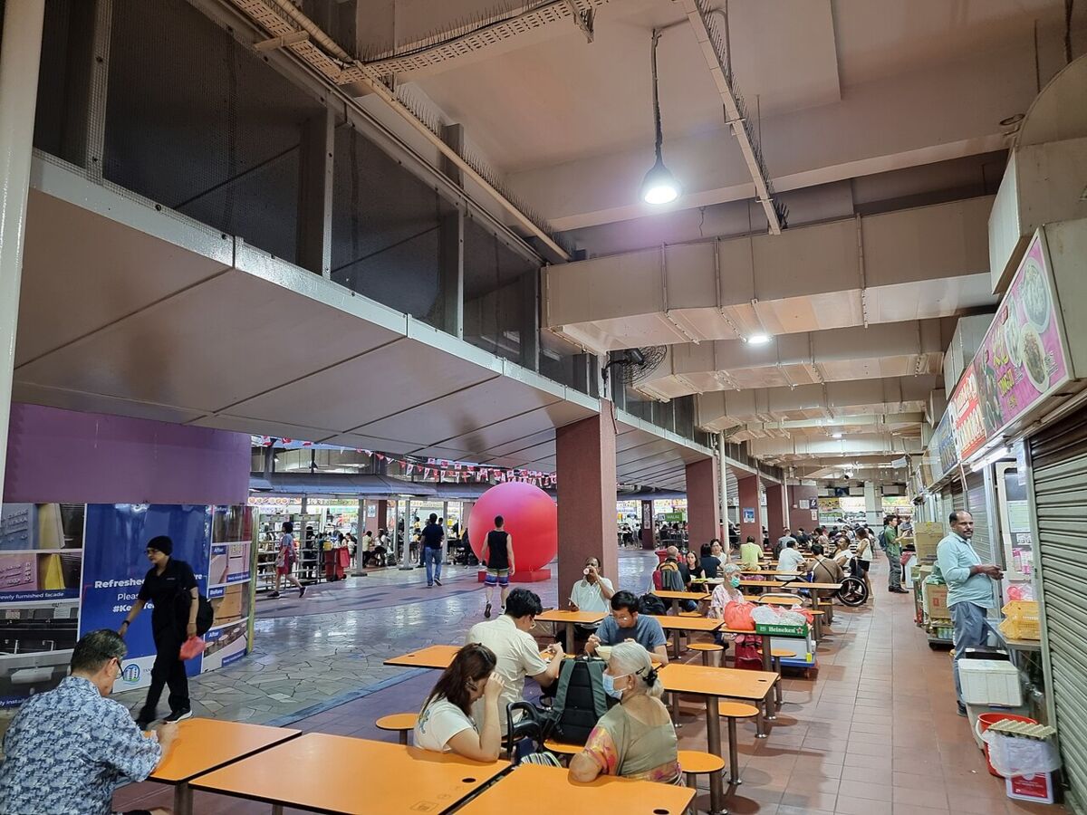 Indoor dining area at Tekka Centre with orange tables and people eating near food stalls