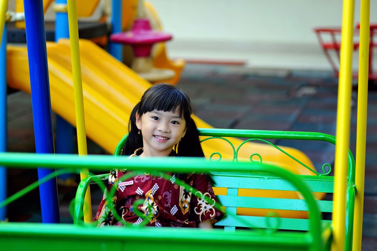 Happy young girl smiling on a green swing at a vibrant playground.