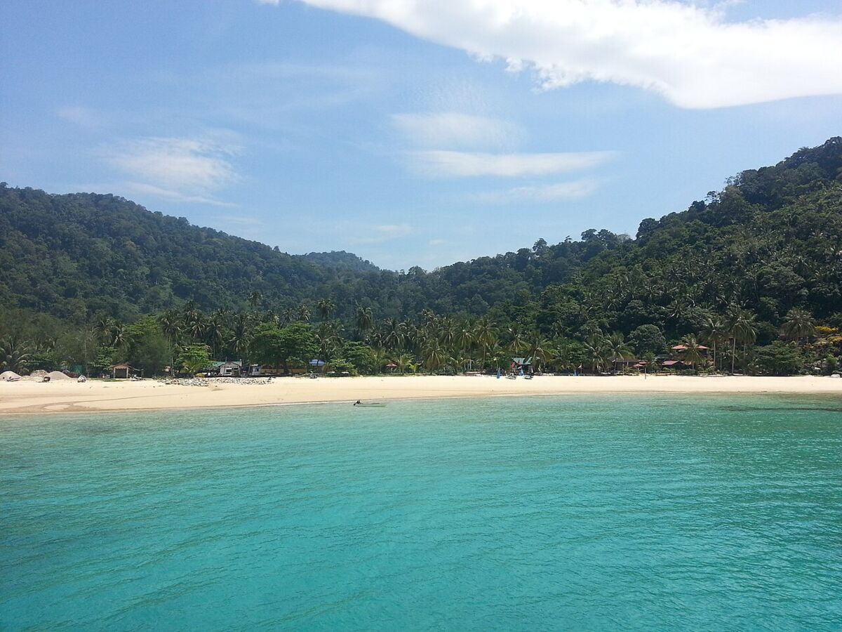 Turquoise water and white sand at Salang beach on Tioman Island, backed by jungle hills and palm trees