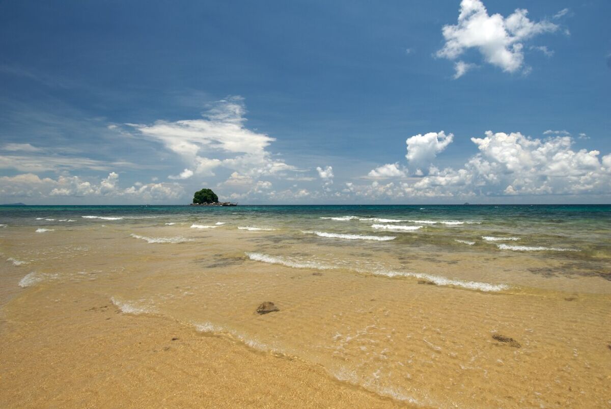 Shallow clear water lapping a sandy Tioman beach with a small tree-topped islet on the horizon