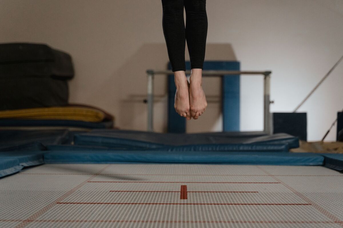 Athlete jumping on trampoline indoors, captured mid-air with focus on legs.