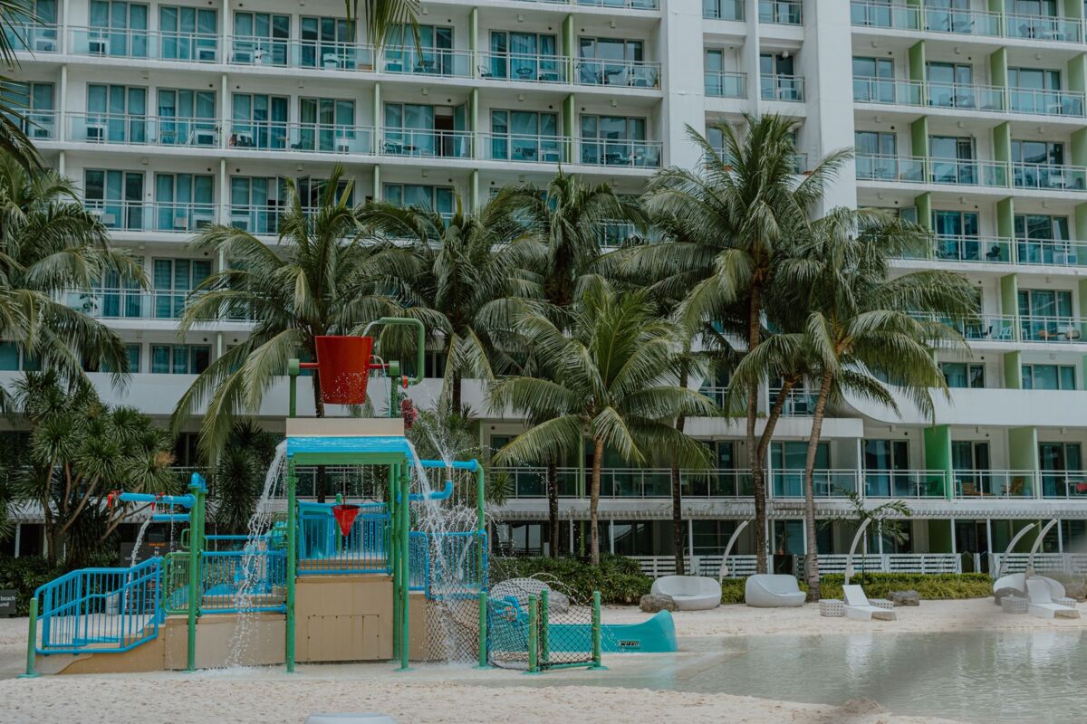 A modern resort featuring a children's water play area surrounded by lush palm trees and beachfront views.