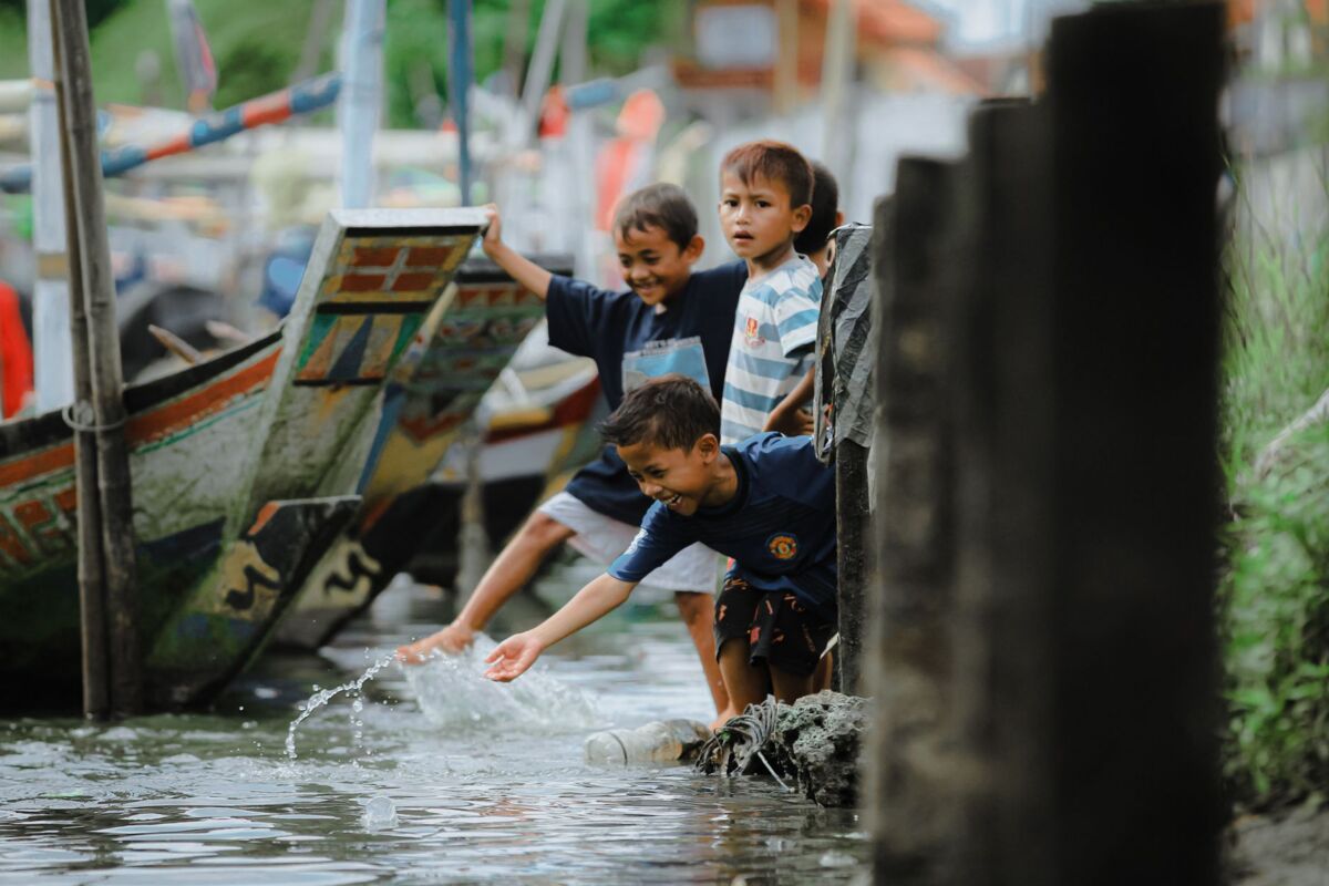 Children enjoying water play beside traditional boats in East Java, Indonesia.