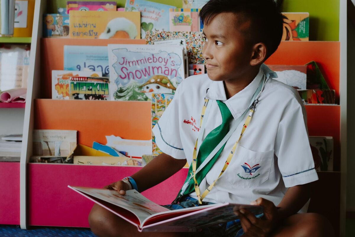 A young boy in a school uniform reads joyfully in the library, promoting education and learning.