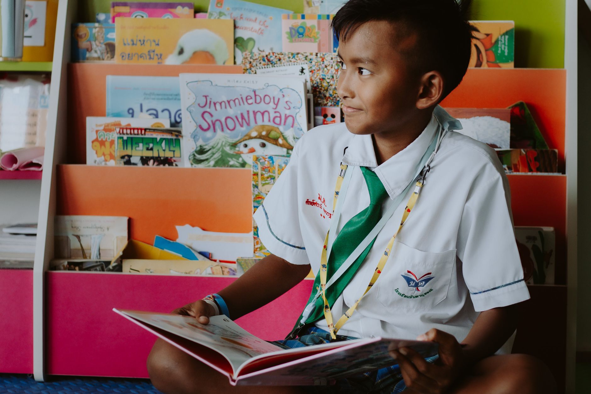 A young boy in a school uniform reads joyfully in the library, promoting education and learning.