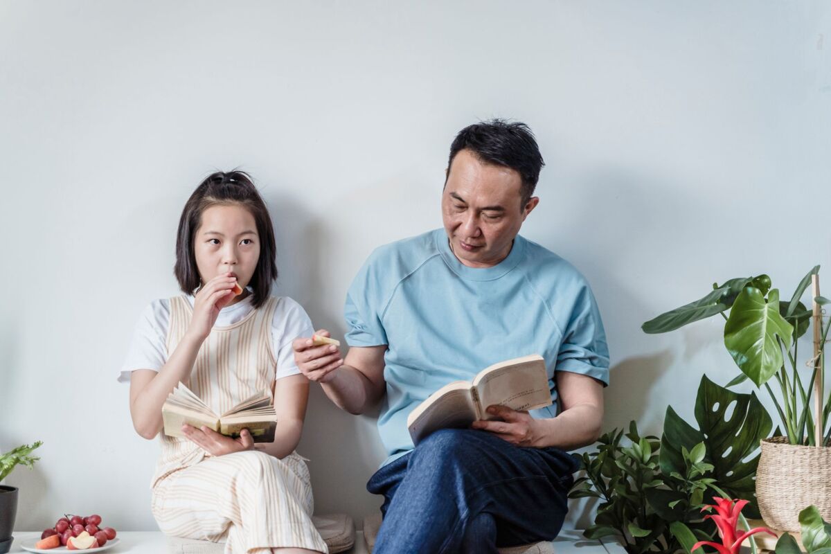 Asian father and daughter enjoying a quiet reading time indoors surrounded by plants.