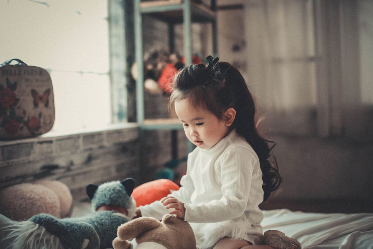 Adorable Asian child playing with stuffed toys indoors, showcasing innocent childhood moments.