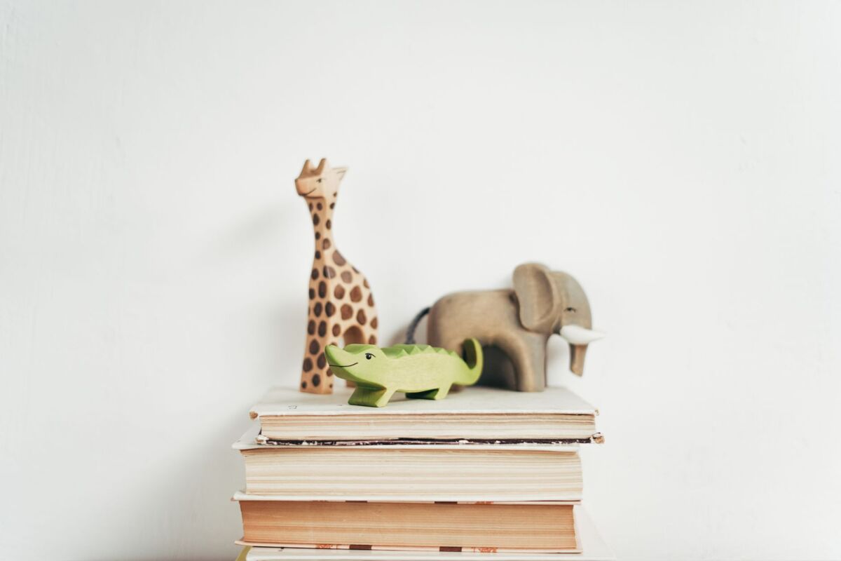 Stack of books with wooden toy giraffe, elephant, and crocodile on a white background. Ideal for educational themes.